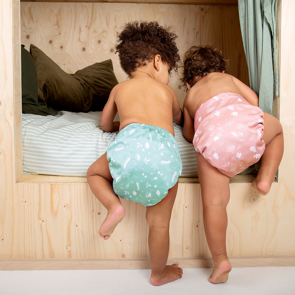 two babies wearing TotsBots nappies climbing onto a wooden shelf