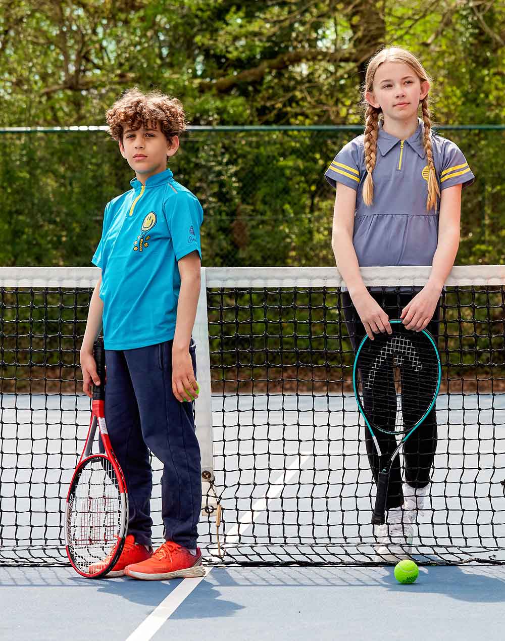 A young boy and girl stood on a tennis court