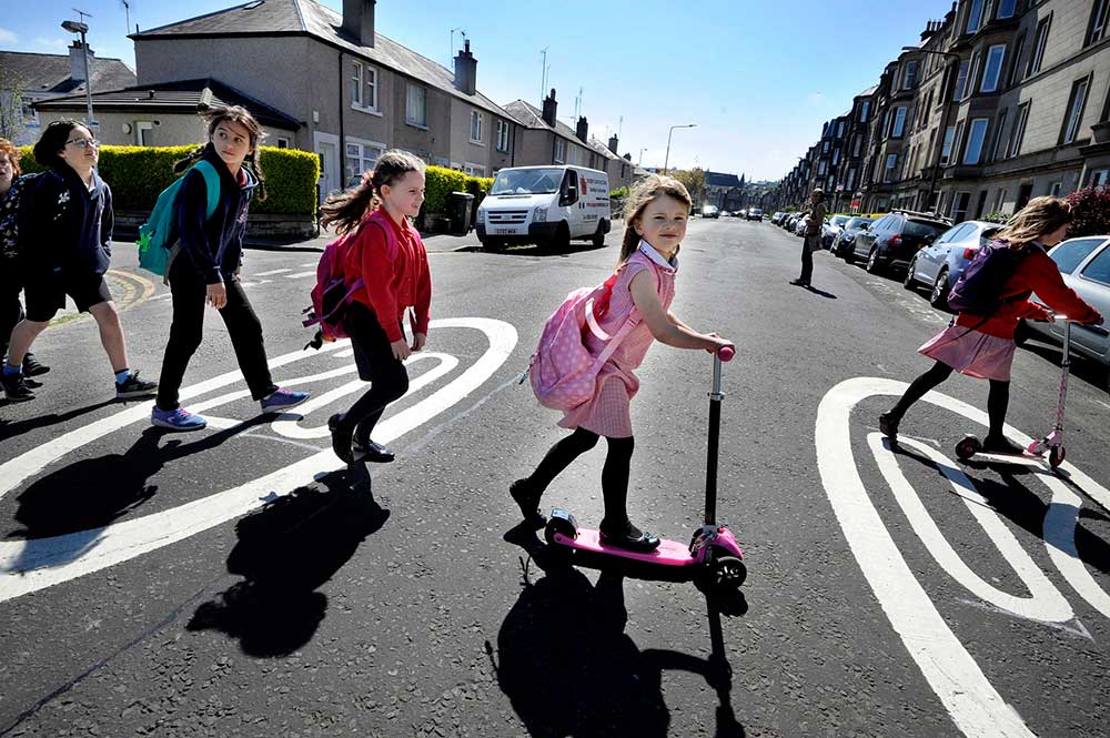 A group of children walking and riding their scooters to school