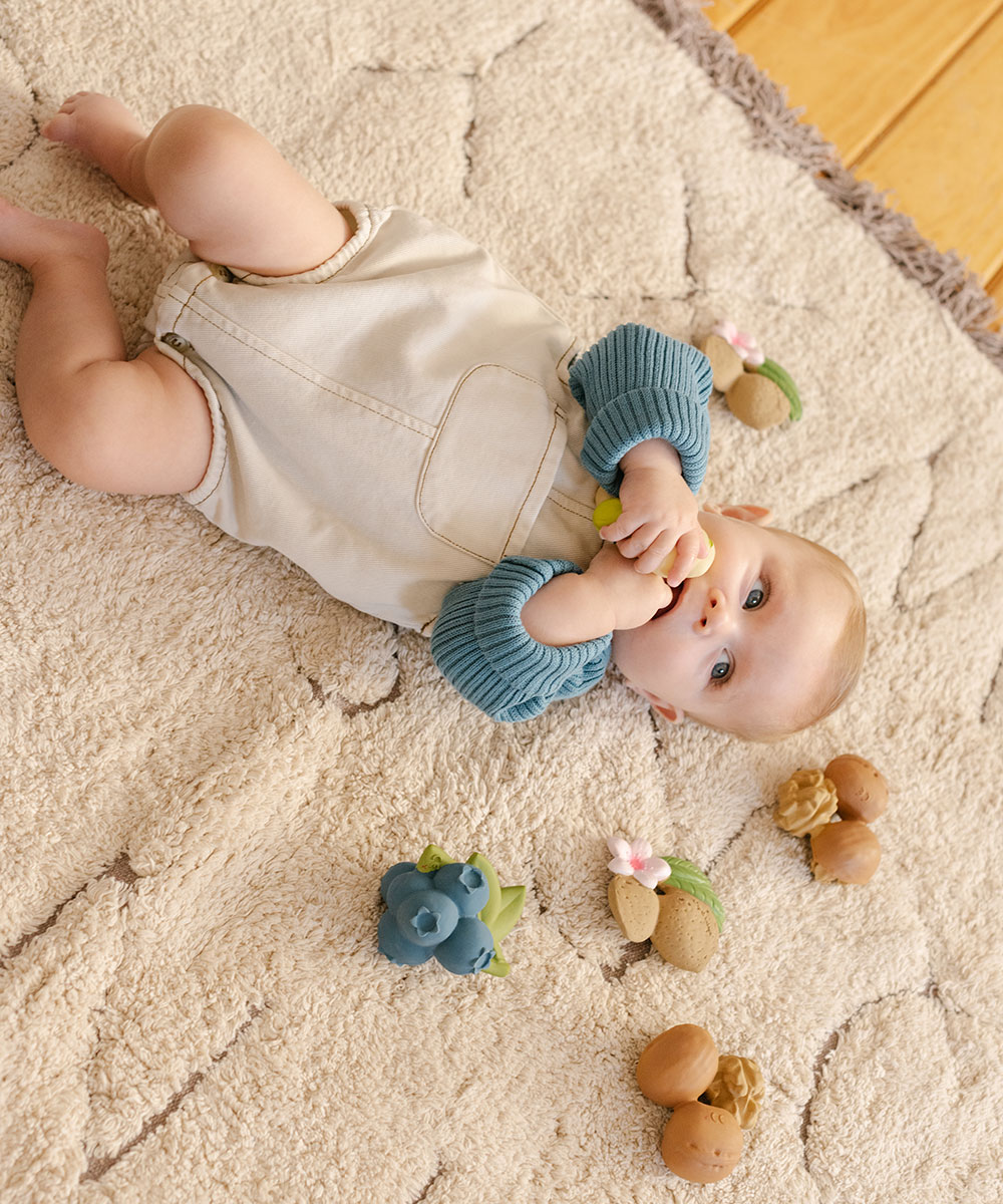 Baby laid on a rug playing with Oli&Carol Nuts and Forest Fruits collection