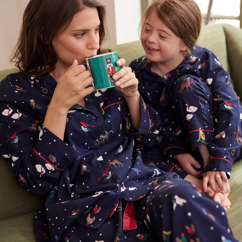 mum drinking a cup of tea, sat with daughter in matching Joules Christmas pyjamas