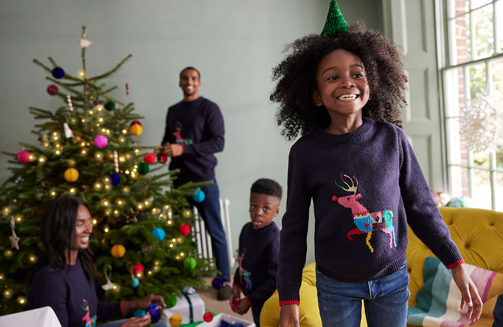 Familiy around christmas tree wearing Joules christmas jumpers - Joules trading update