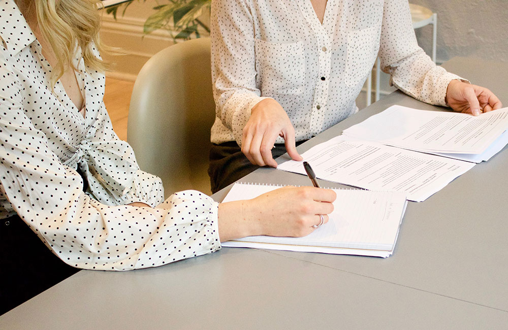 Two ladies in office writing on paper