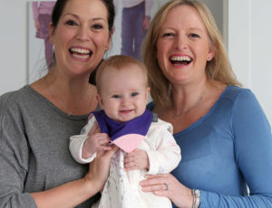 Two women holding a baby with a cheeky chompers teething bib - Next online