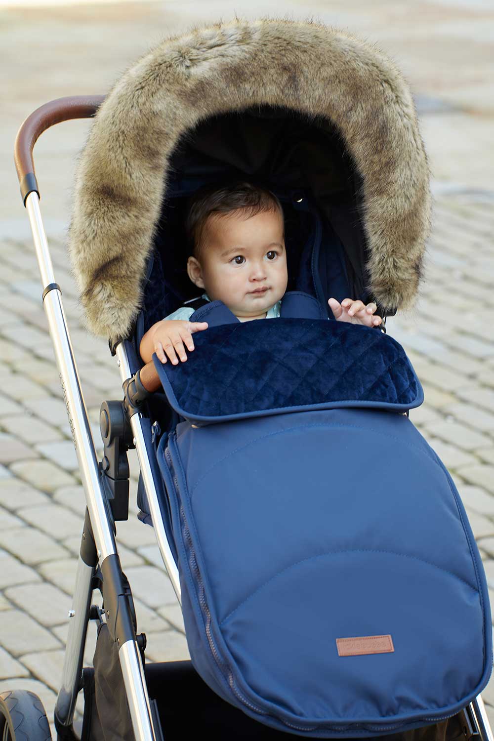 A baby sat in a pushchair with the Ickle Bubba Faux Fur Hood Trim