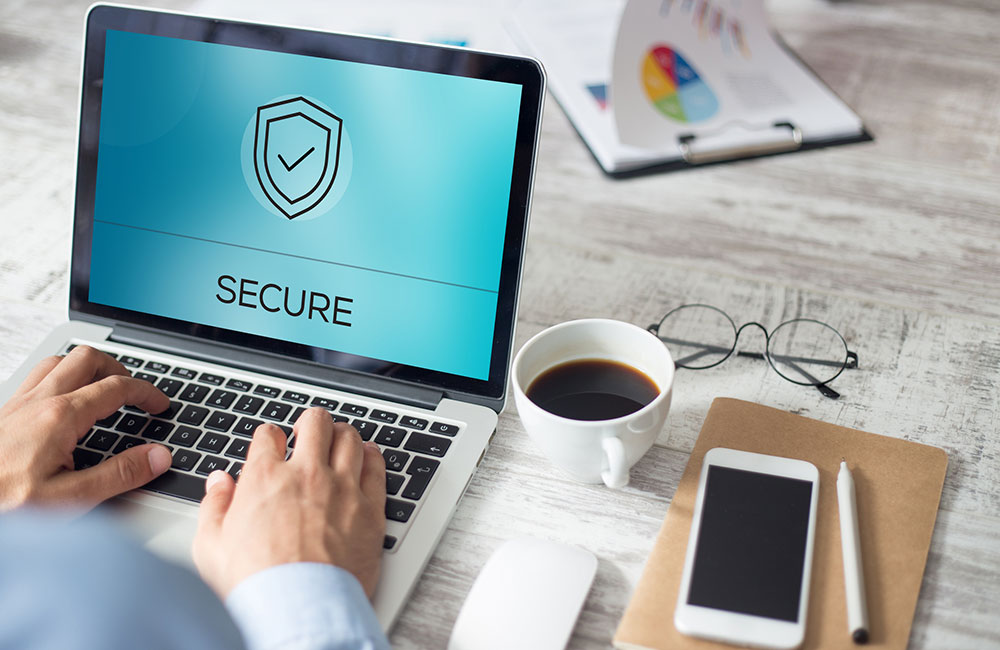 Image of laptop on work desk next to coffee and phone for cybersecurity story