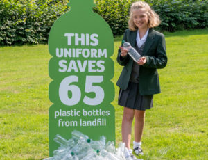 Schoolgirl in grren Trutex uniform stood next to plastic bottle recycling sign