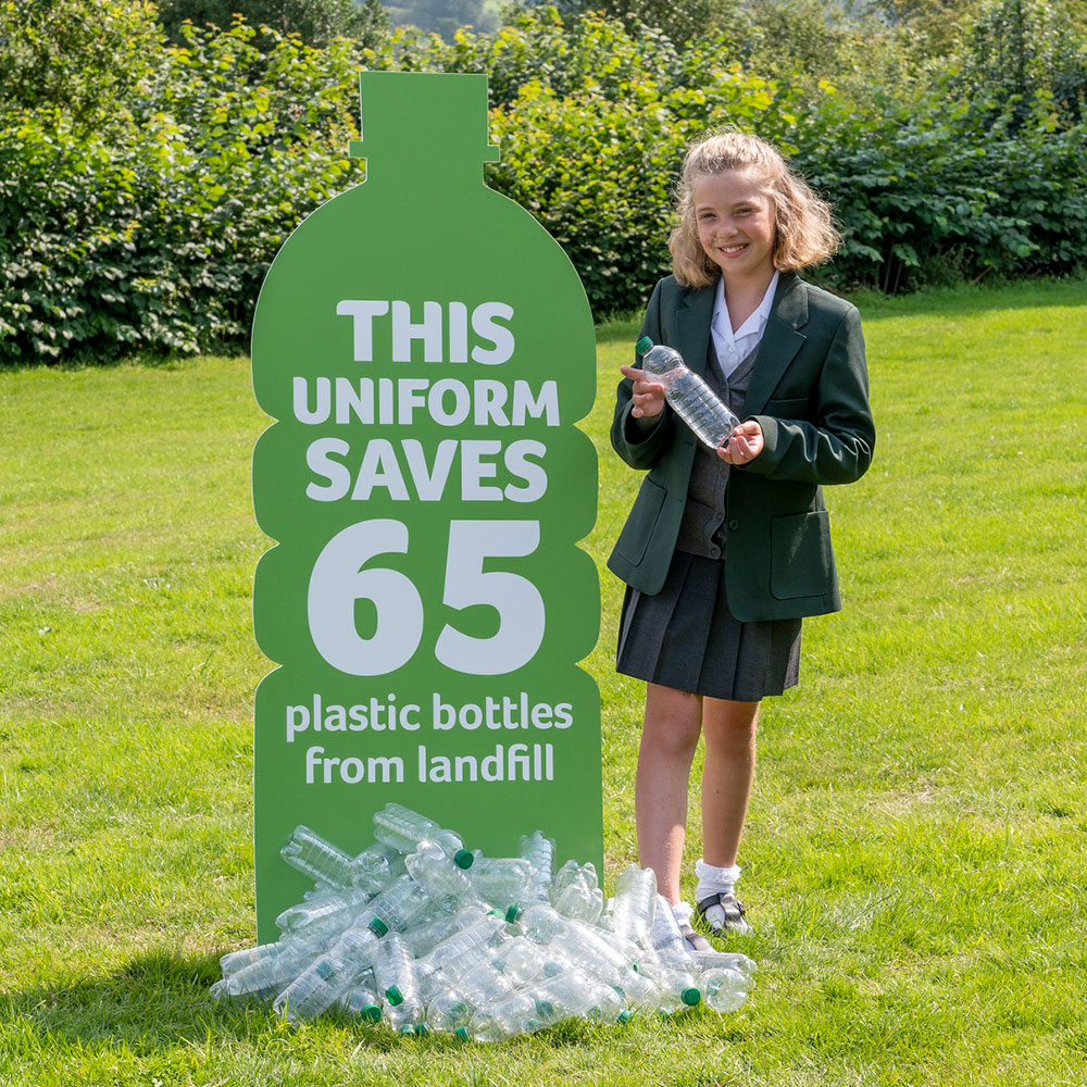 Schoolgirl in grren Trutex uniform stood next to plastic bottle recycling sign