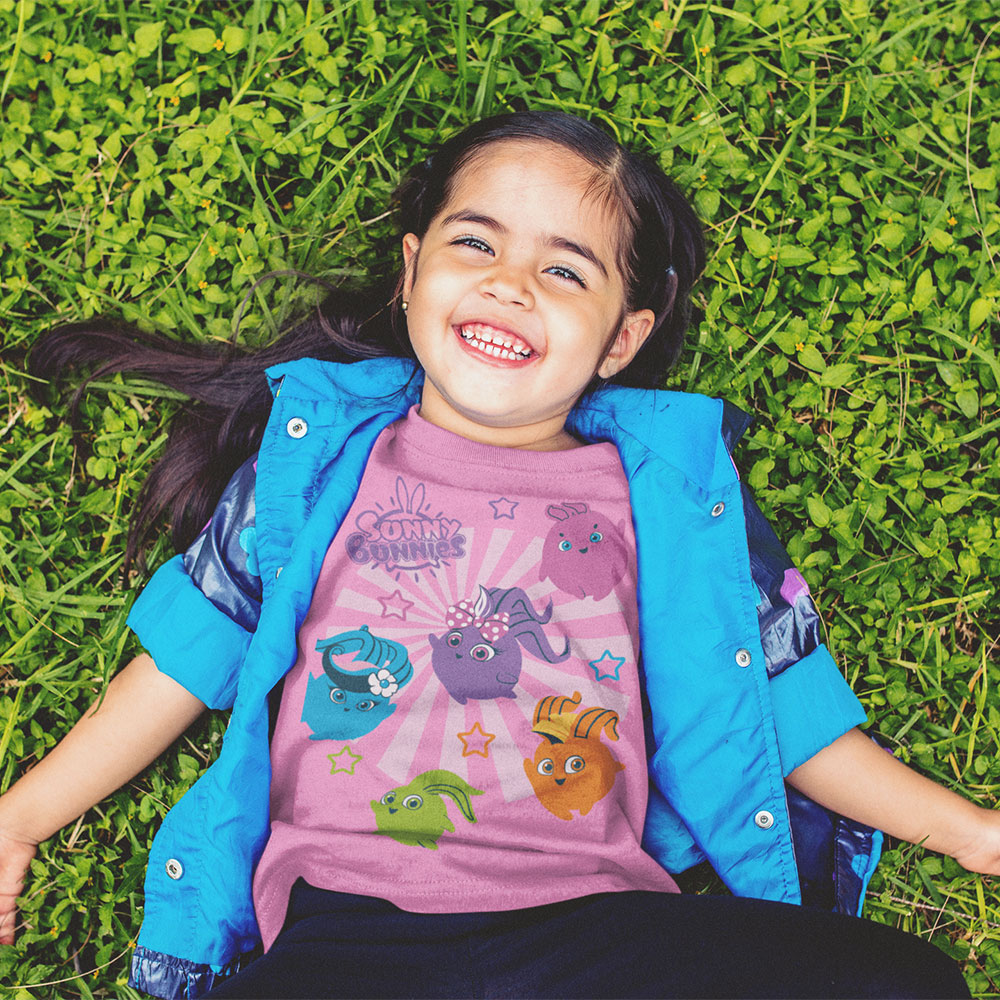 Young girl laid in grass smiling with Sunny Bunnies branded T Shirt on