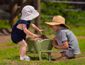 Boy and girl playing in the grass with small green Bobux gardening wheelbarrow