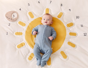 baby boy laid on yellow sun nursery mat with numbers around