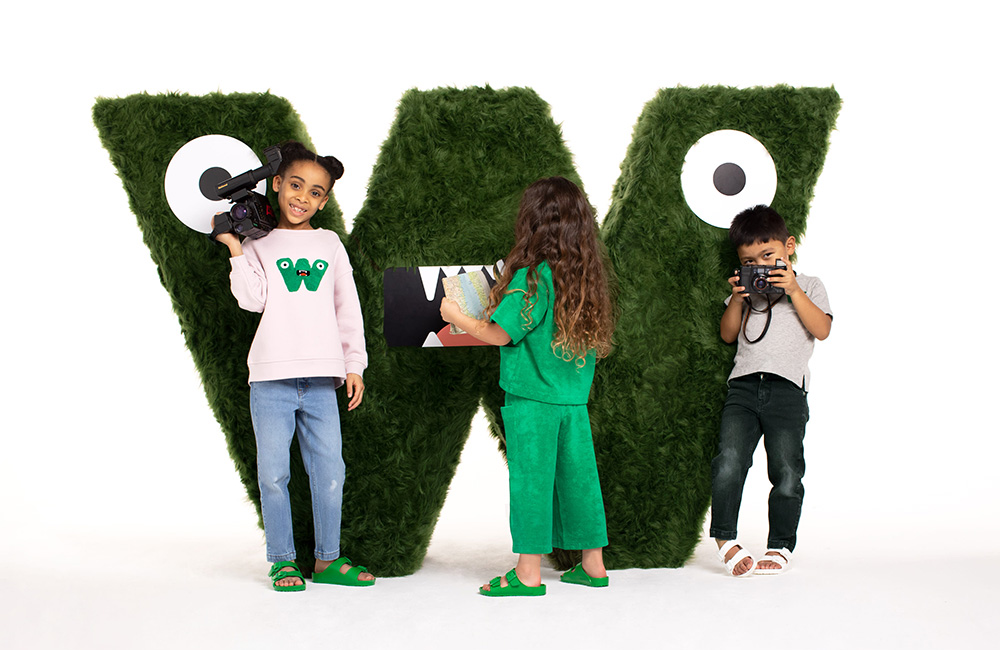 Three children stood next to a large W logo wearing Whistles kidswear