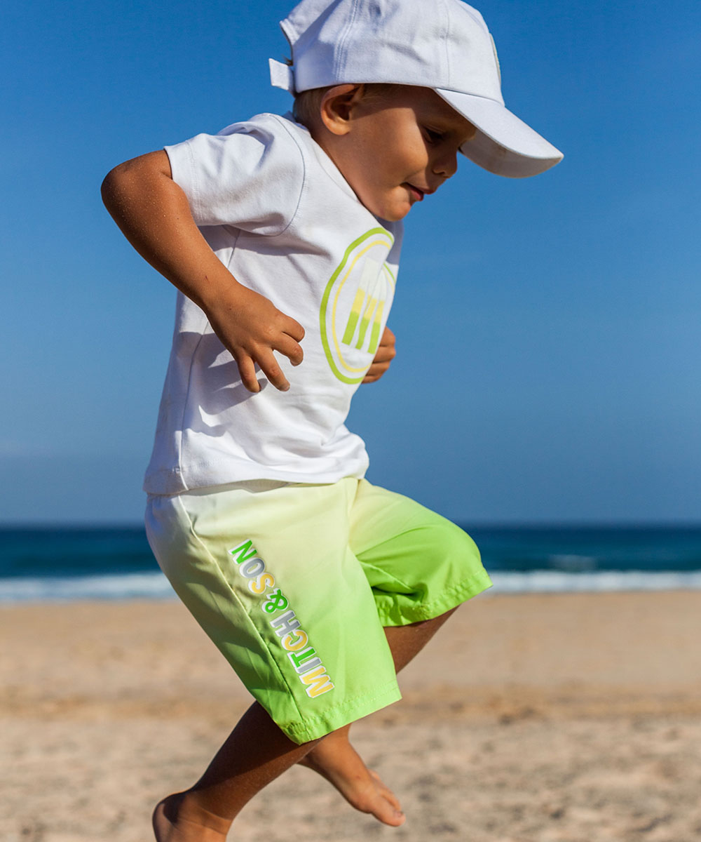 Boy jumping on beach wearing shorts and T-shirt by Picture Book Fashion 