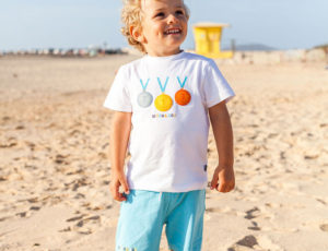 Boy stood on beach in shorts and T-shirt by Picture Book Fashion