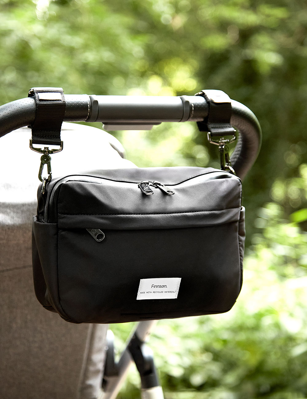 A black cross-body bag hanging from the handle of a pram