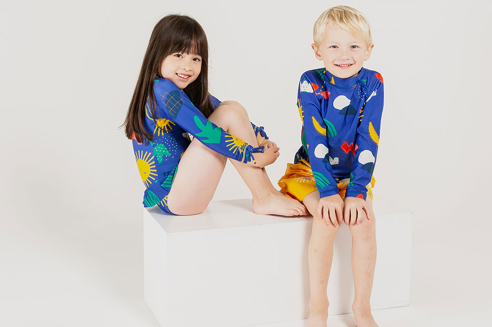 A boy and girl sat down wearing bright coloured swimwear