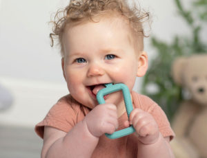 Baby with curly hair biting on cheeky chompers teething ring