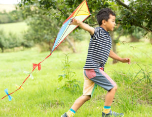 A young boy running through a field with a kite in his hand