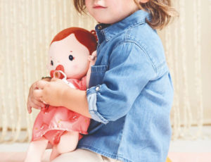 A young girl kneeling down on the floor holding a rose doll in her arms