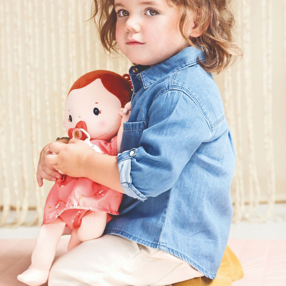 A young girl kneeling down on the floor holding a rose doll in her arms