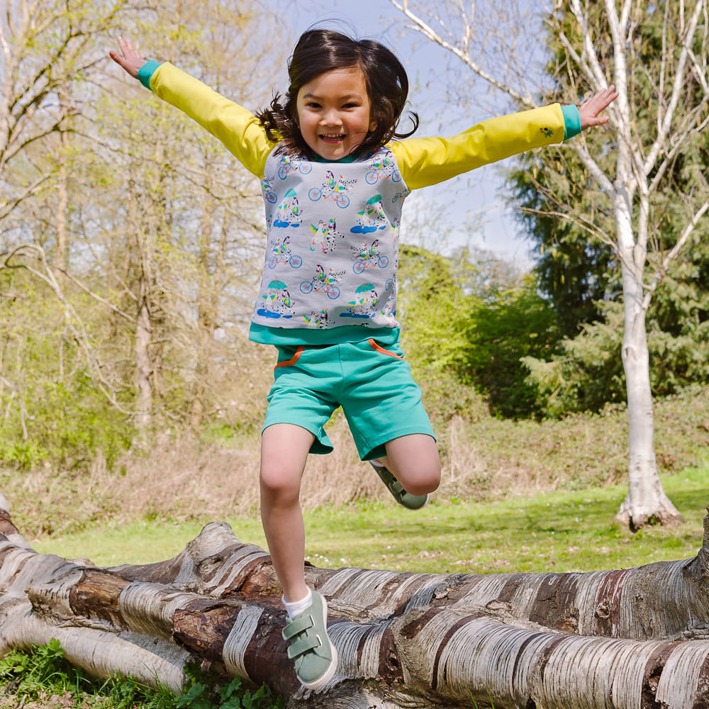 Girl jumping with arms outstretched, wearing ducky zebra colourful clothing