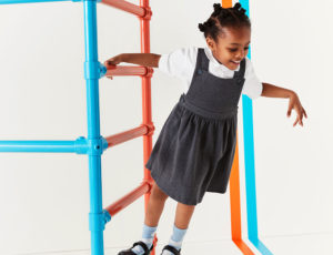 young school girl on orange and blue climbing framce wearing school uniform