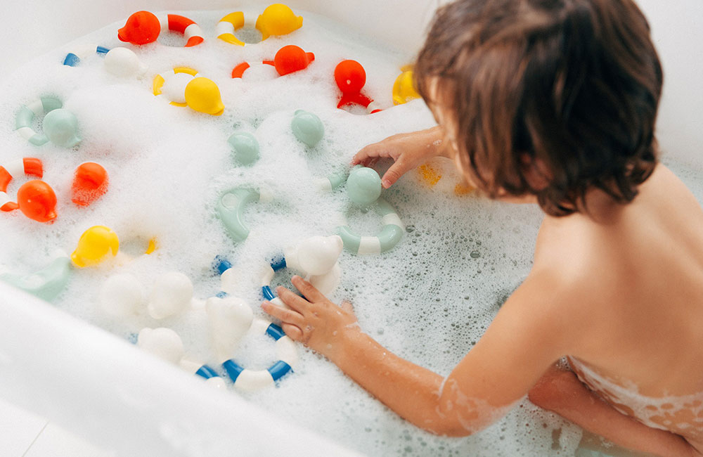 Young boy in bath plaing with Oli&Carol colourful bath toys