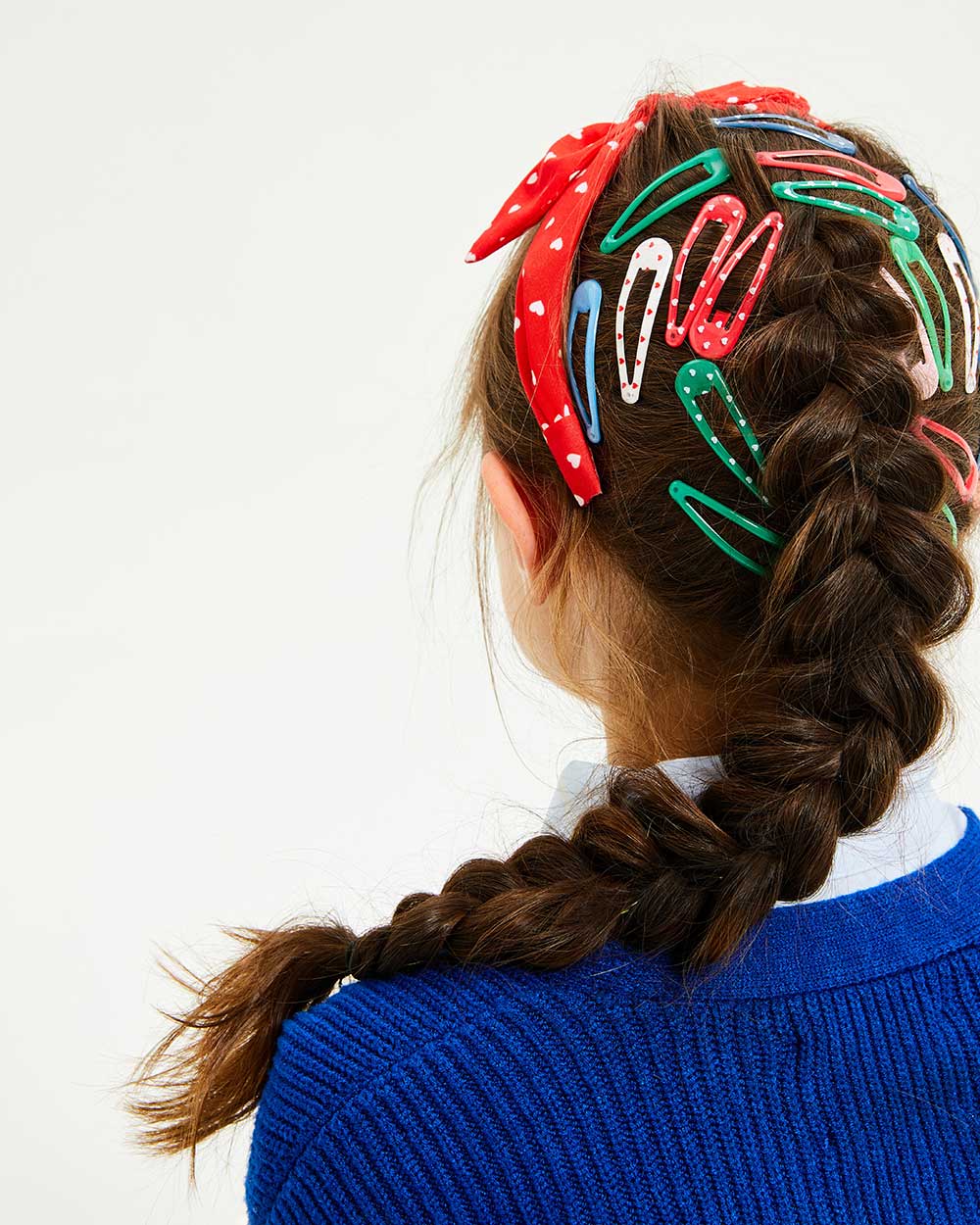 A young girl in a blue jumper wearing accessories in her hair