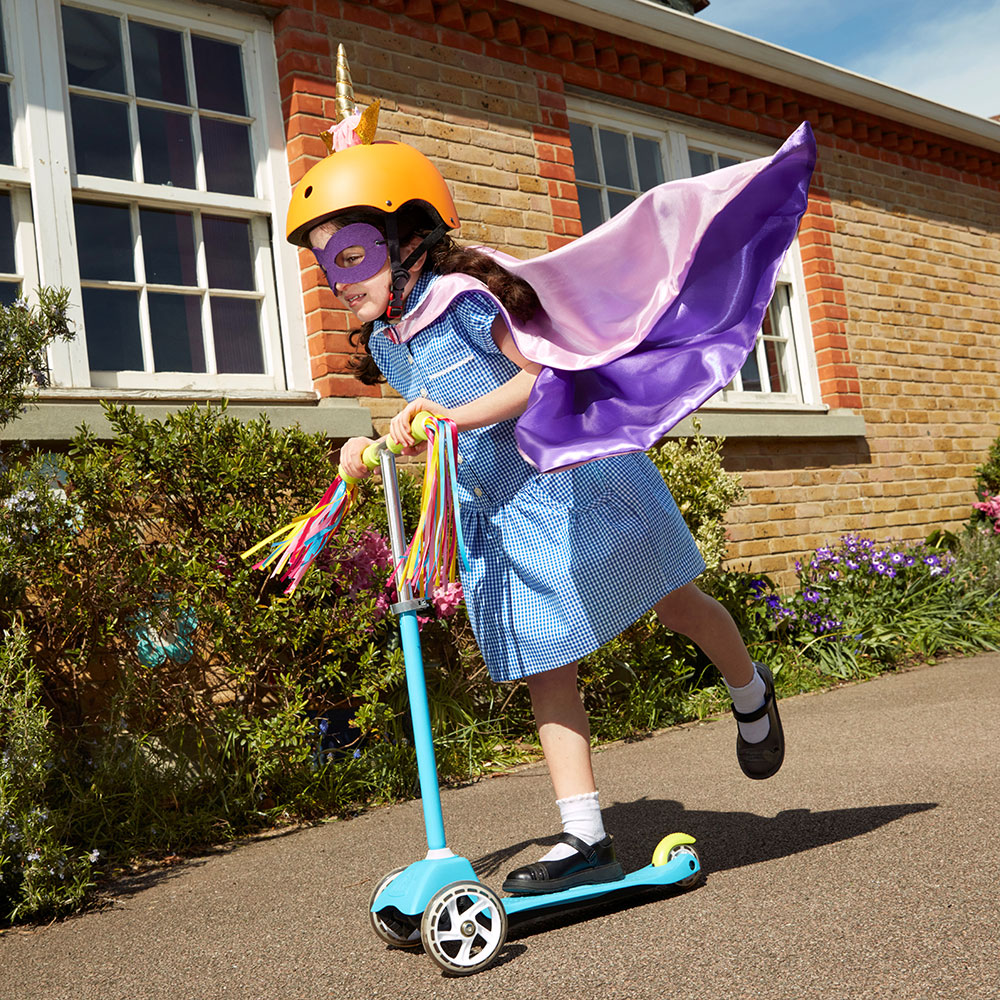 Girl in school uniform on scooter wearing mask and cape
