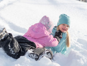 children playing in the snow wearing pink and aqua penguin snowsuit