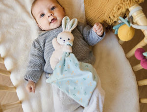 Baby laid in crib with a Carré Douceur soft comforter toy rabbit