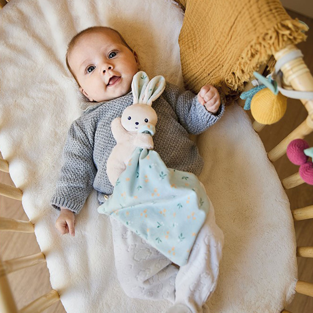 Baby laid in crib with a Carré Douceur soft comforter toy rabbit