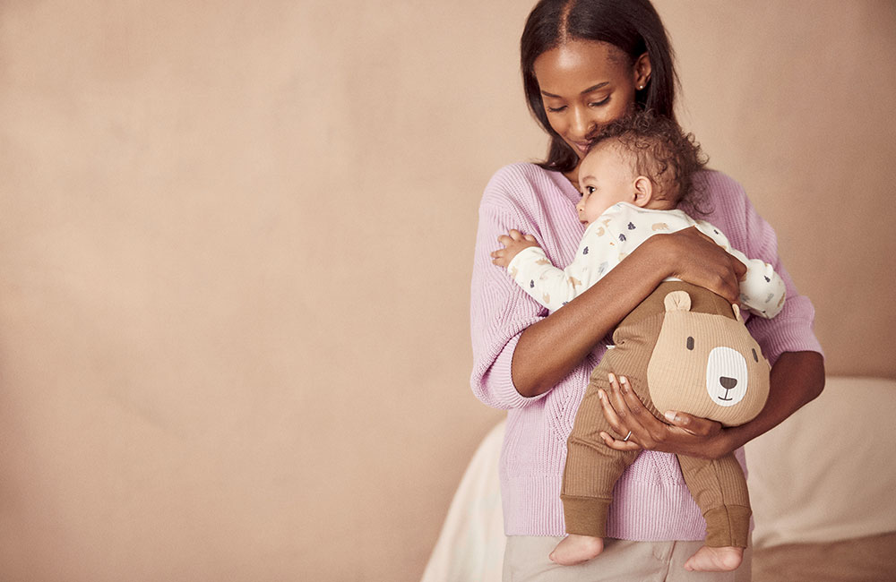 mother holding baby wearing brown Autumn Bear babygro