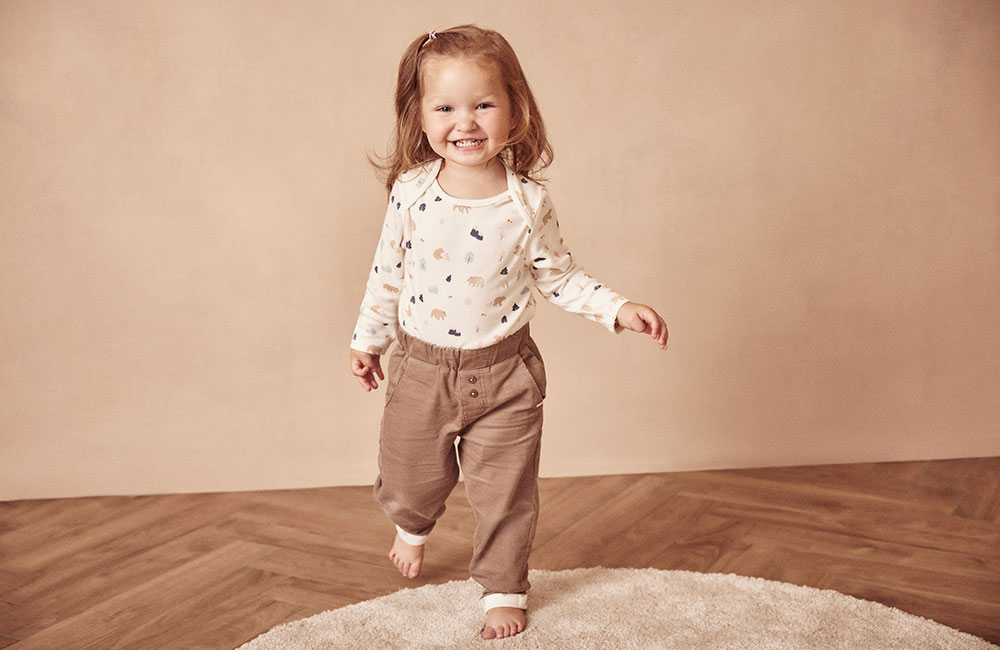 young girl in beige t shirt with Autumn Bear motif and brown trousers
