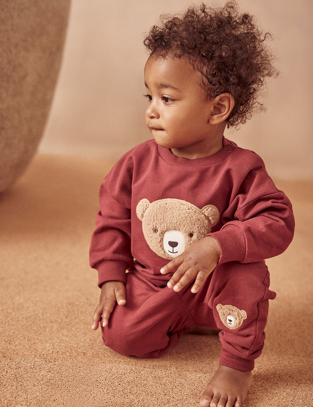 baby boy in dark red pyjamas with Autumn Bear on front and leg