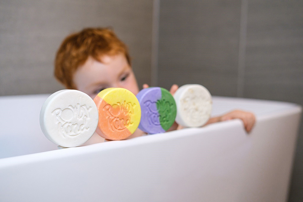 A young boy sat in the bath with four bath soaps