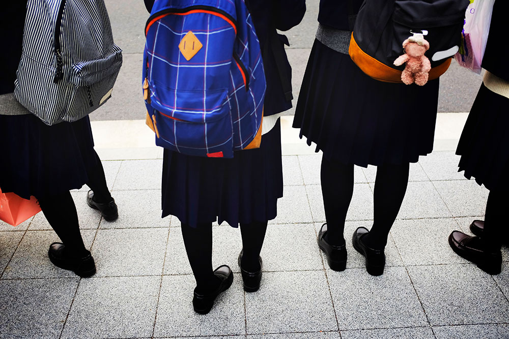 Four school kids in school uniform with a backpack on their back
