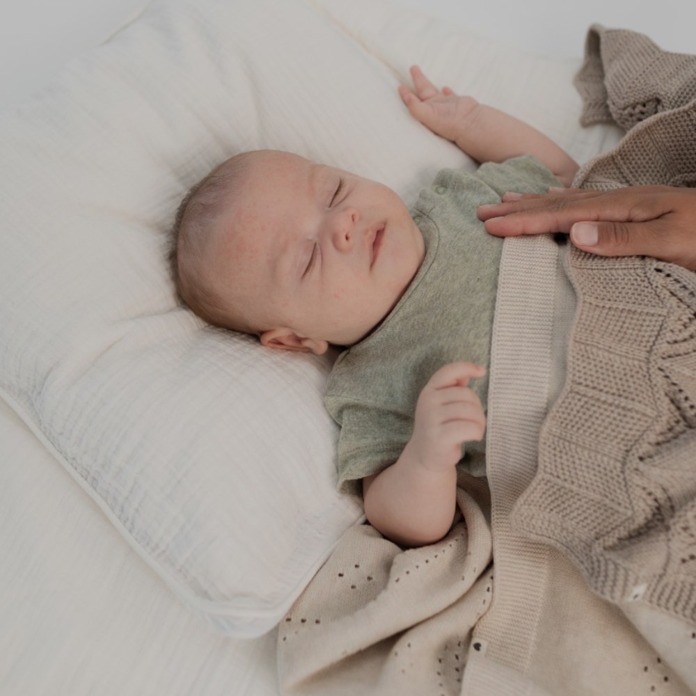 Baby lying down covered by knitted blankets by BIBS