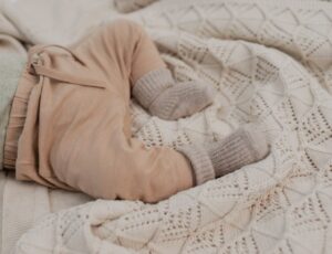 Baby's legs and body show lying on a knitted BIBS baby blanket
