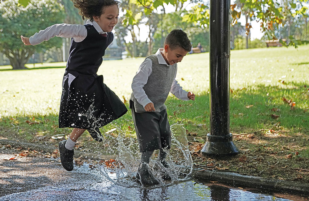 Girl and boy dressed in school uniform jumping in a puddle