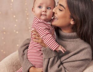 Woman holding a bearing wearing a festive red and whiite striped babygro from Borro
