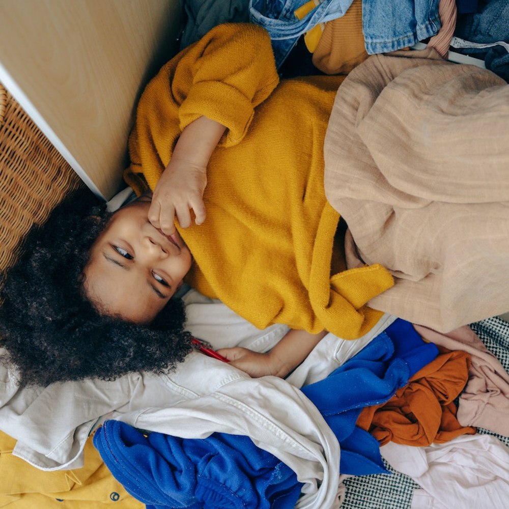 Child lying in a pile of clothes beside a wardrobe