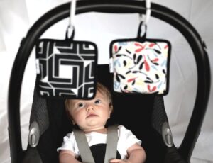 Baby is a carrier looking up at sensory squares hanging from the handle