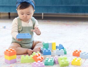 Baby sat on the floor in front of a blue sofa playing with a toy building block play set by Infantino