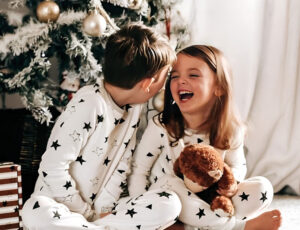 Two children sat in front of a Christmas tree wearing Jammie Doodle Christmas Eve pyjamas