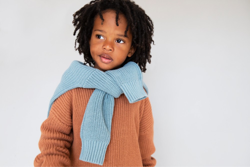 Child wearing a brown knitted Kidly jumper with a pale blue jumper tied across his shoulders