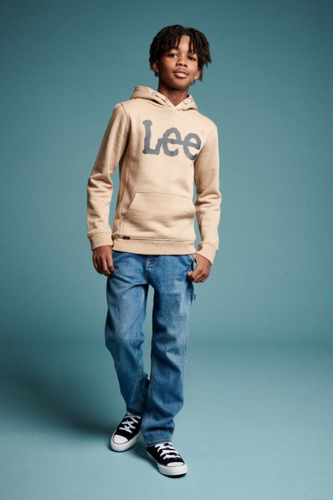 Boy stood against a blue background wearing Lee Jeans 