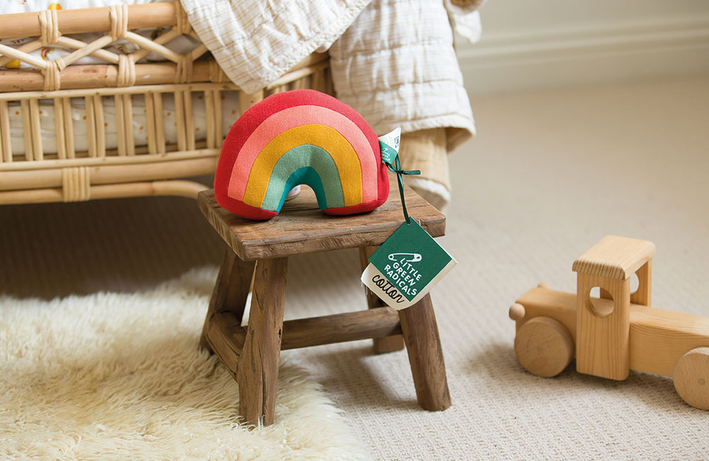 Little Green Radicals rainbow soft toy on a wooden stool
