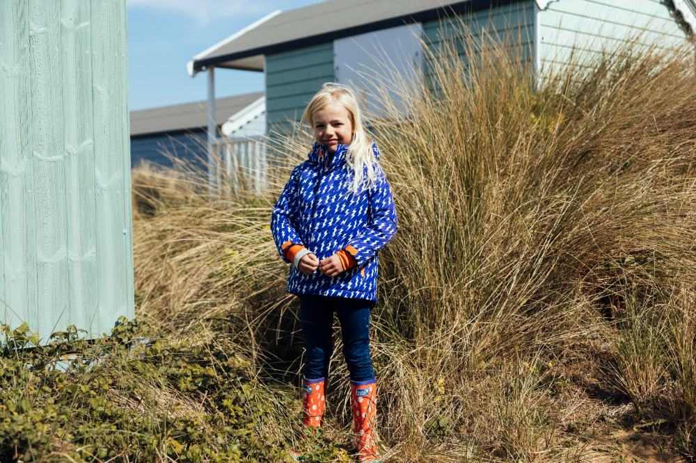 Girl stood by a beach hut wearing Muddy Puddles outerwear and wellies 