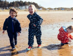 Three children stood on beach wearing Muddy Puddles outerwear